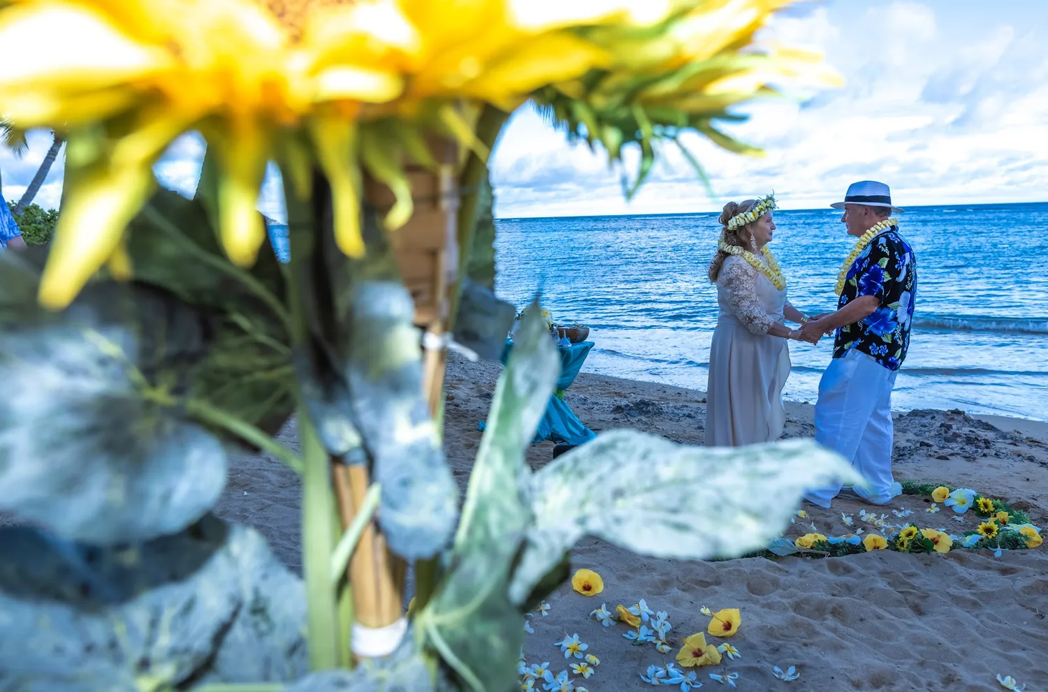 Yellow flowers in the foreground as the couple stands at the water