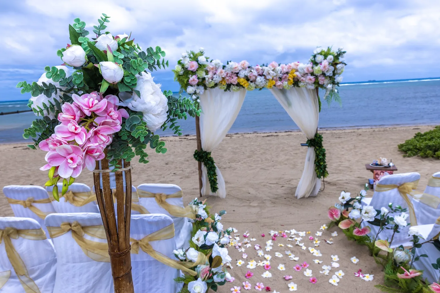 Pink and white floral stand beside the aisle with the arch and ocean behind