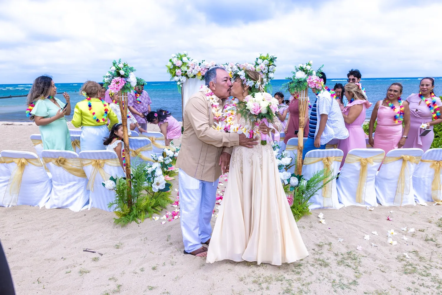 Rose and Carl holding hands under the white and blue flower arch by the ocean