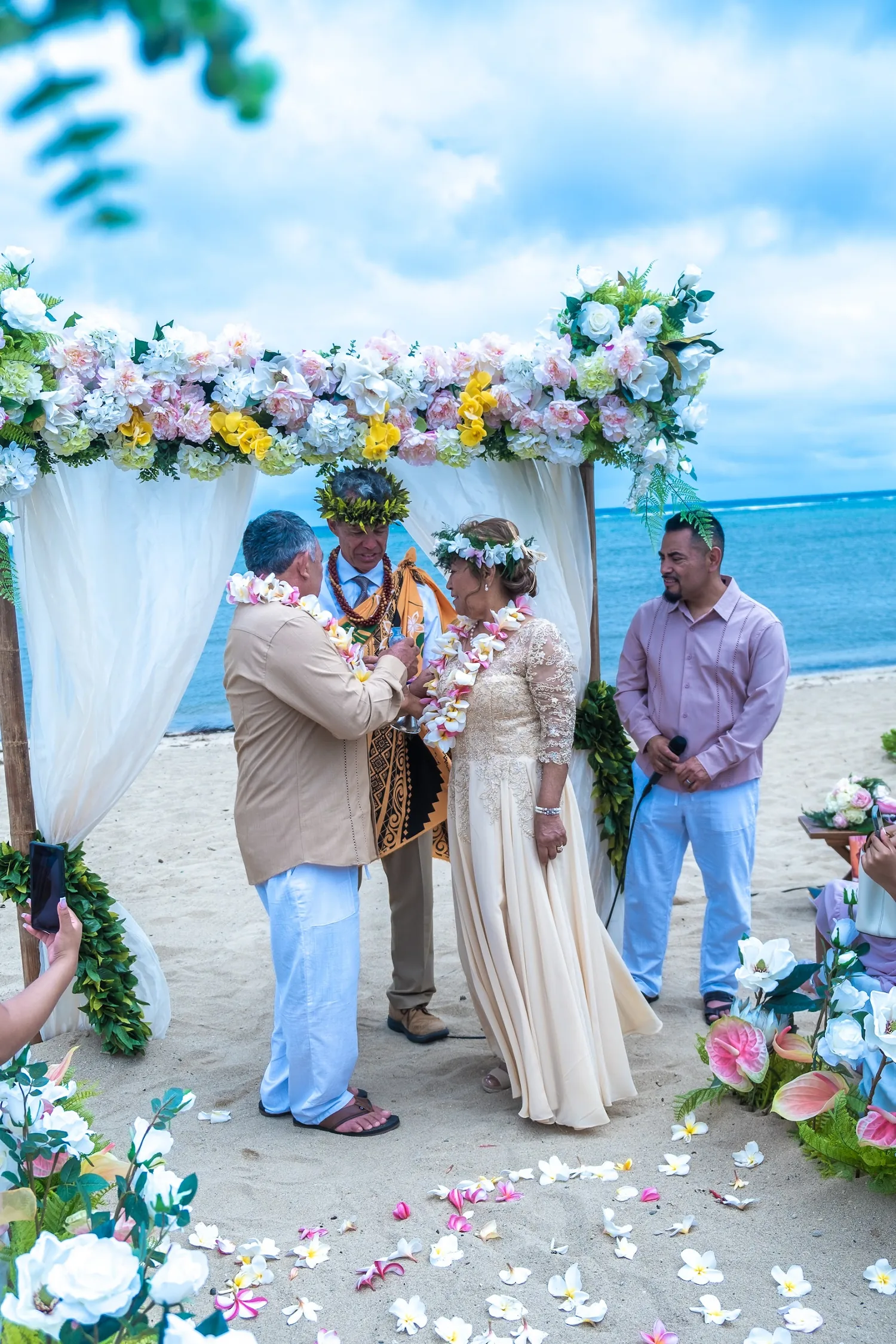 Saying their vows under a white draped arch with yellow and white flowers