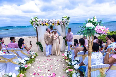 The couple at the flower arch with family seated by the ocean