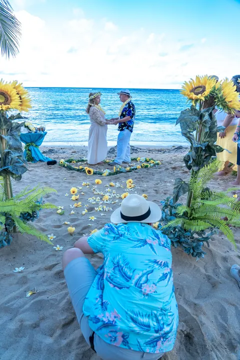 A yellow plumeria heart on the sand with the couple behind