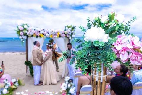A tall white floral arrangement at the end of the aisle as the couple stands at the arch