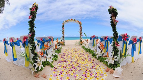 A white trellis arch and flower aisle on the long white sand beach