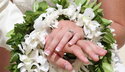Their wedding rings on maile and white orchid leis