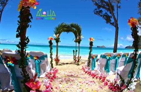 The green palm frond archway with tiki torches and tropical flowers on the sand at Waimanalo