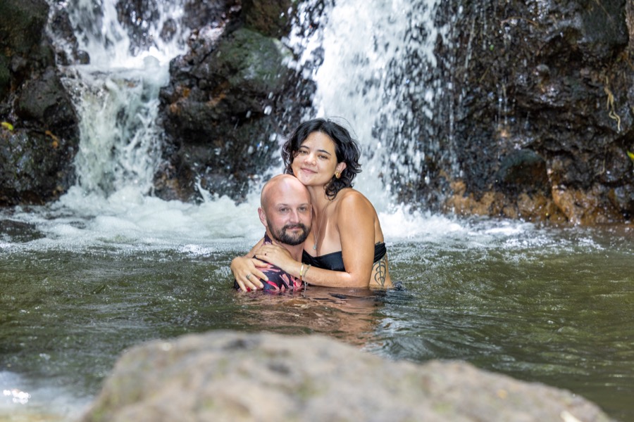 Couple hugging in the waterfall pool with the falls behind them