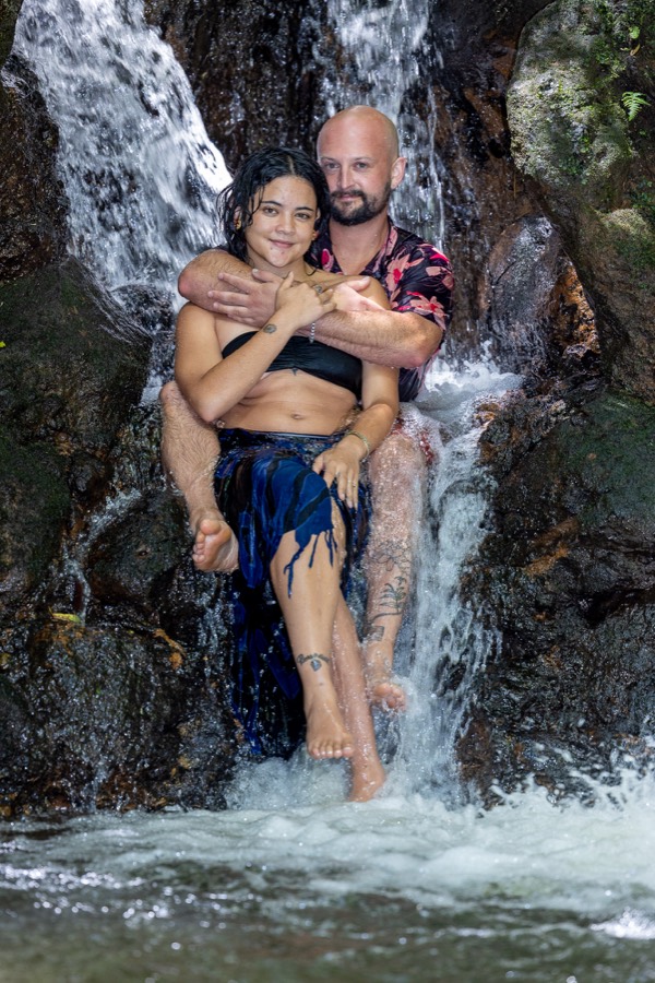 Couple sitting together in the cascading water of a Nuuanu waterfall