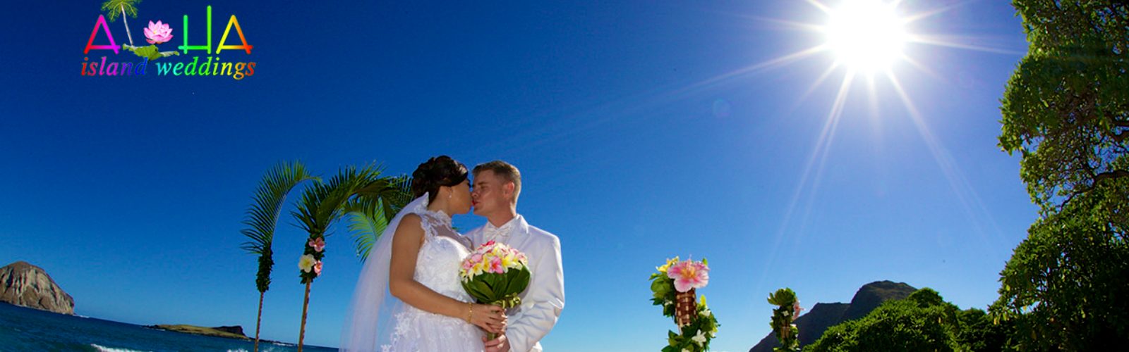 Bride and groom kissing under a flower arch on an Oahu beach